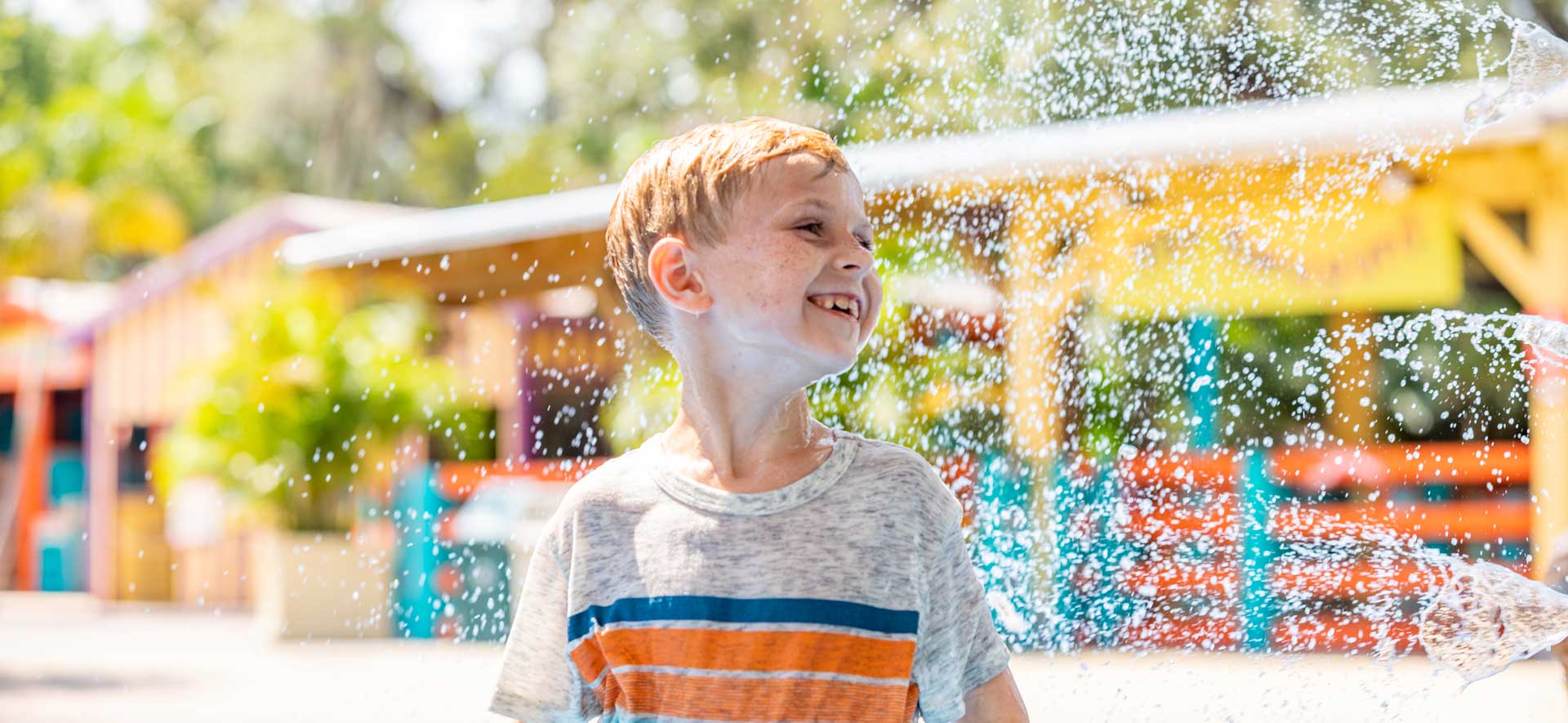 Boy looking to his left, smiling while getting misted by one of the splashpad water features